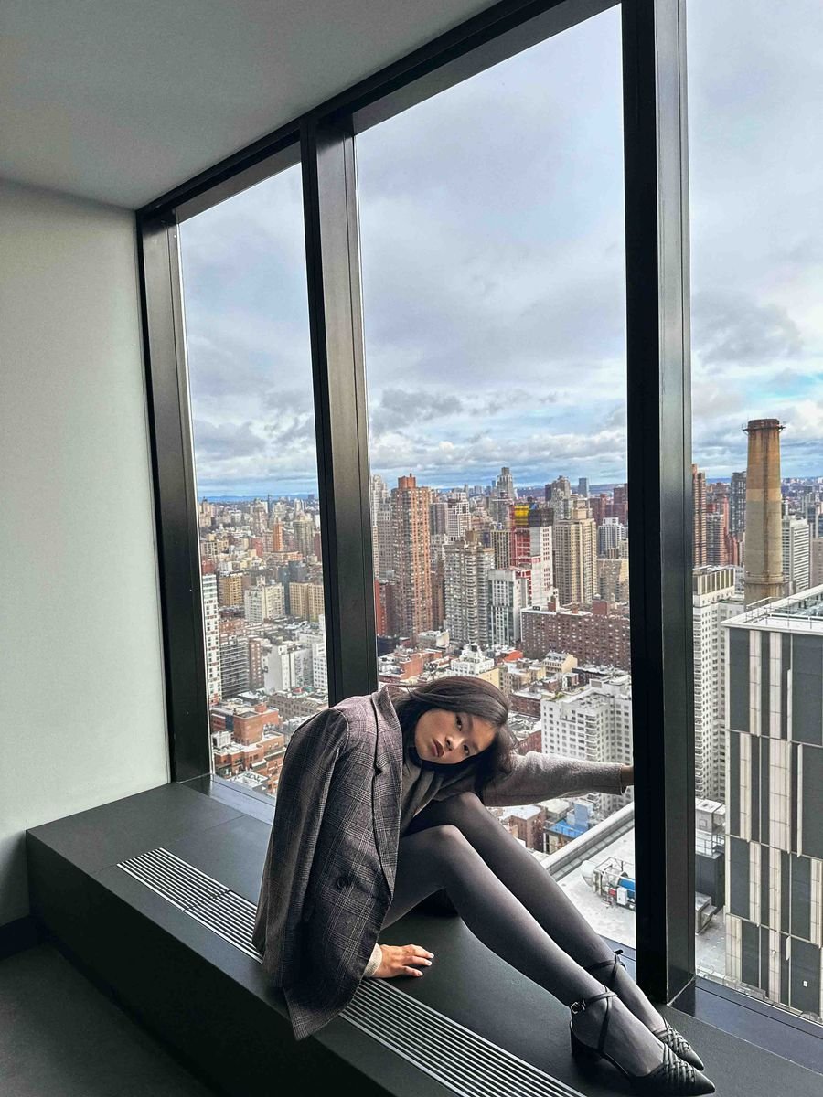 Model on a high-rise window seat with a wide city skyline behind her